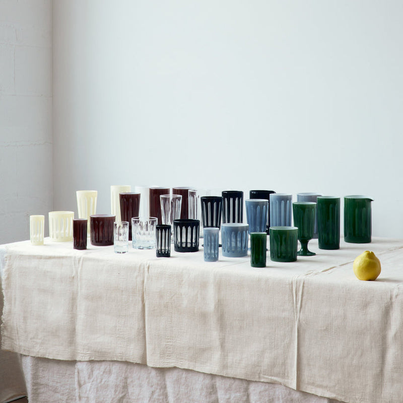 Sir|Madam | Empire Glacier Nips Glasses, Set of 4, elegantly displayed on a draped table, showcasing varied silhouettes inspired by 1920s skyscrapers, complemented by a lemon.