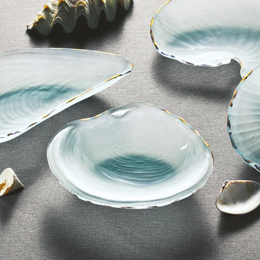 Annie Glass | 8 x 8.5 Shells Clam - Frosted Gold dish, featuring a clam shell shape with gold edging, displayed among small shell fragments on a fabric surface.