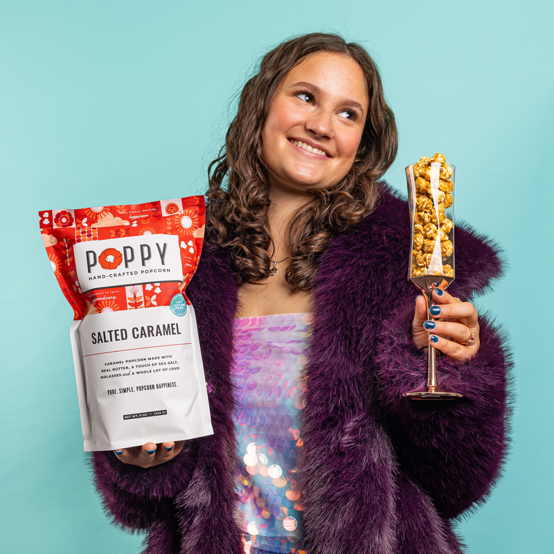 Woman holding Poppy | Handcrafted Popcorns - Salted Caramel bag and glass, highlighting its handcrafted, gluten-free, Non-GMO qualities.