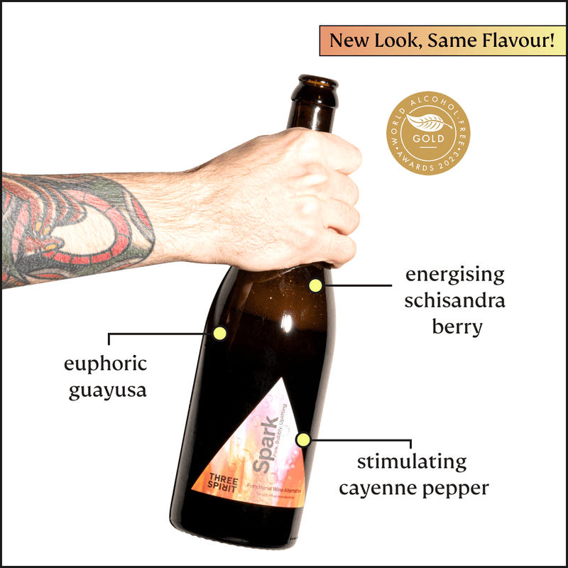Three Spirit Blurred Vines Spark bottle held by a tattooed arm, featuring New Look, Same Flavour! banner. Highlights guayusa, schisandra berry, and cayenne. World Alcohol-Free Awards 2023 seal.