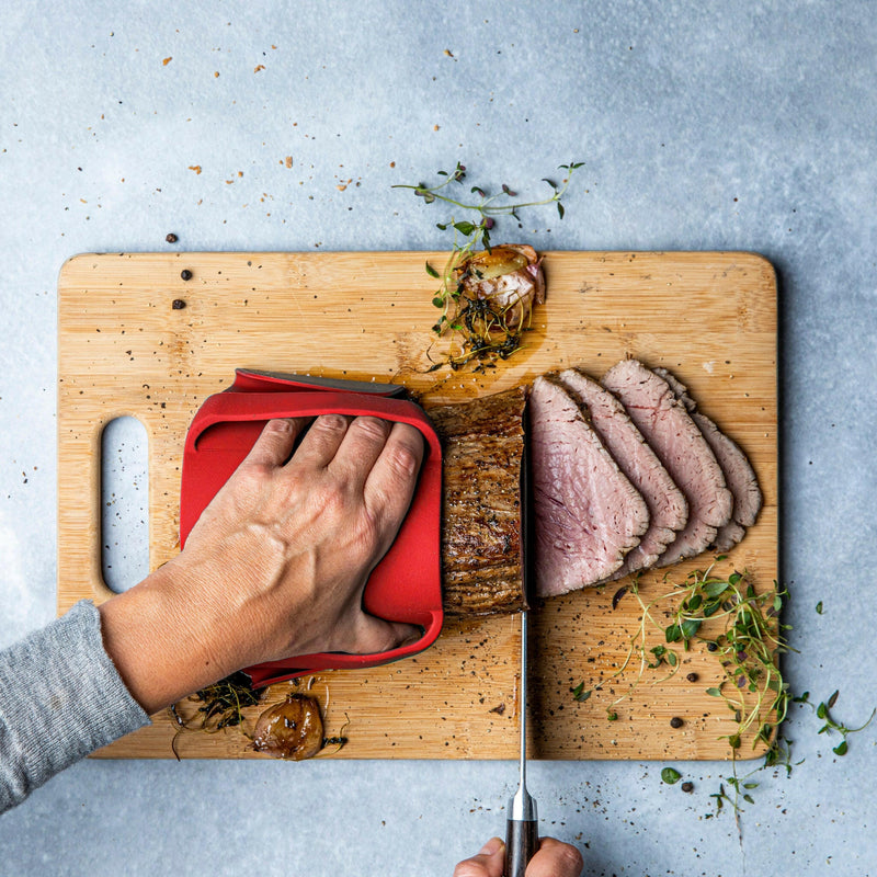 Person using WOW GEAR | Gripmitt - Green to safely slice meat on a cutting board, highlighting its versatile kitchen use for handling foods.
