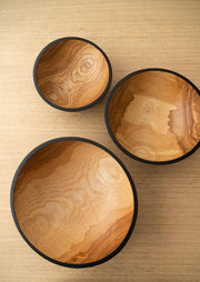 Creating Comfort Lab | Handmade Ukrainian Charred Wooden Salad Bowls, Medium, set of three nesting bowls with natural wood-grain interiors and dark rims, on a light tabletop.