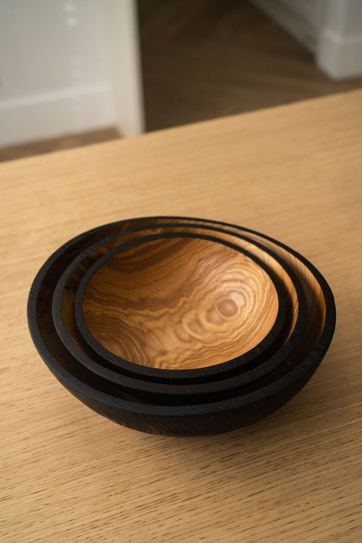 Creating Comfort Lab | Handmade Ukrainian Charred Wooden Salad Bowls, Set of 3, showcasing beautifully figured interiors and a dark-stained exterior, nested on a light wood tabletop.