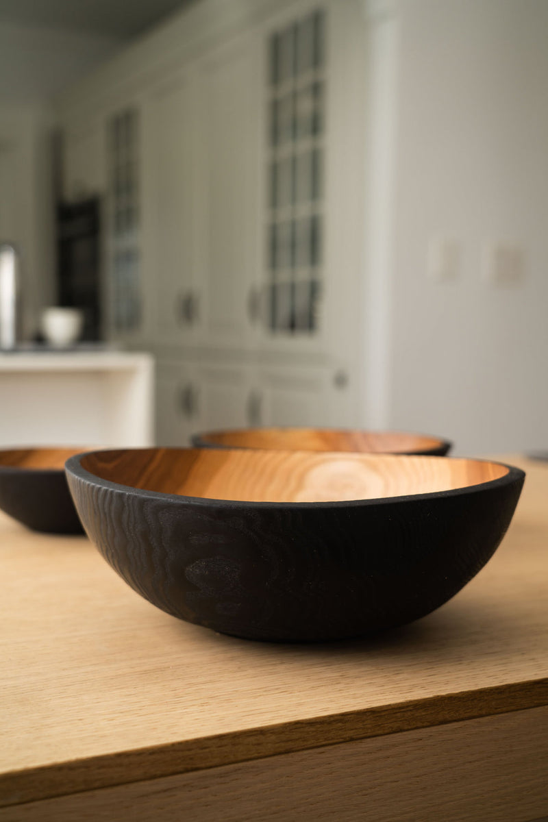 Creating Comfort Lab | Handmade Ukrainian Charred Wooden Salad Bowls, Set of 3, displayed on a light wood countertop, showcasing their distinct charred exterior and natural interior.