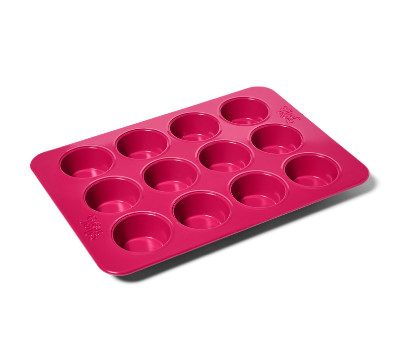 Great Jones | Stud Muffin - Raspberry: Close-up of a pink nonstick, nontoxic muffin pan fitting 12 muffins, ensuring even heat distribution and easy cleanup.