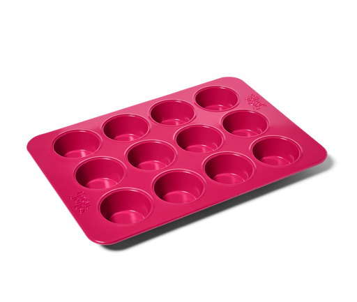 Great Jones | Stud Muffin - Raspberry: Close-up of a pink nonstick, nontoxic muffin pan fitting 12 muffins, ensuring even heat distribution and easy cleanup.