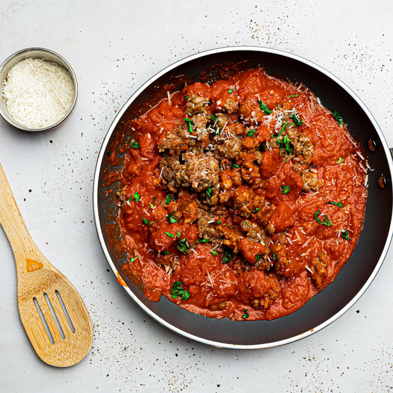 Rock House Creamery Sweet Italian Sausage - 1 lb. - Ground, featuring premium Berkshire pork with housemade spices, alongside a wooden spatula and shredded cheese in a bowl.