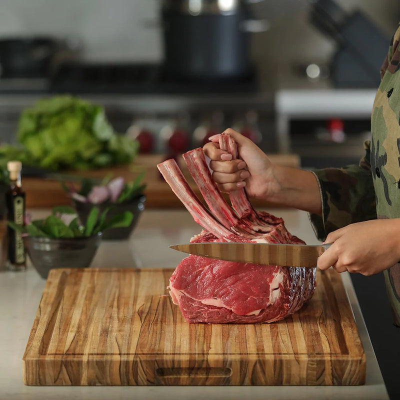 Person slicing meat on the TeakHaus Extra Large Carving Board with Juice Canal, showcasing its stability and spaciousness for large kitchen tasks.