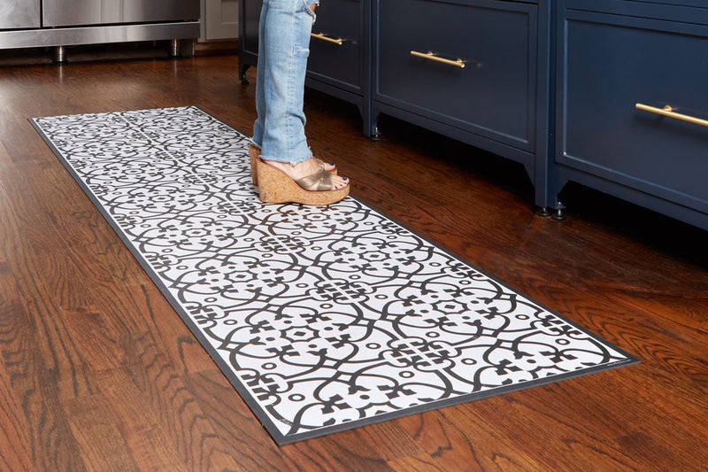 Etú HOME | Liberty L Italian Kitchen Sink Floor Mat (24x47) on hardwood floor by dark blue cabinets, showcasing black-and-white tile pattern in a stylish kitchen setting.