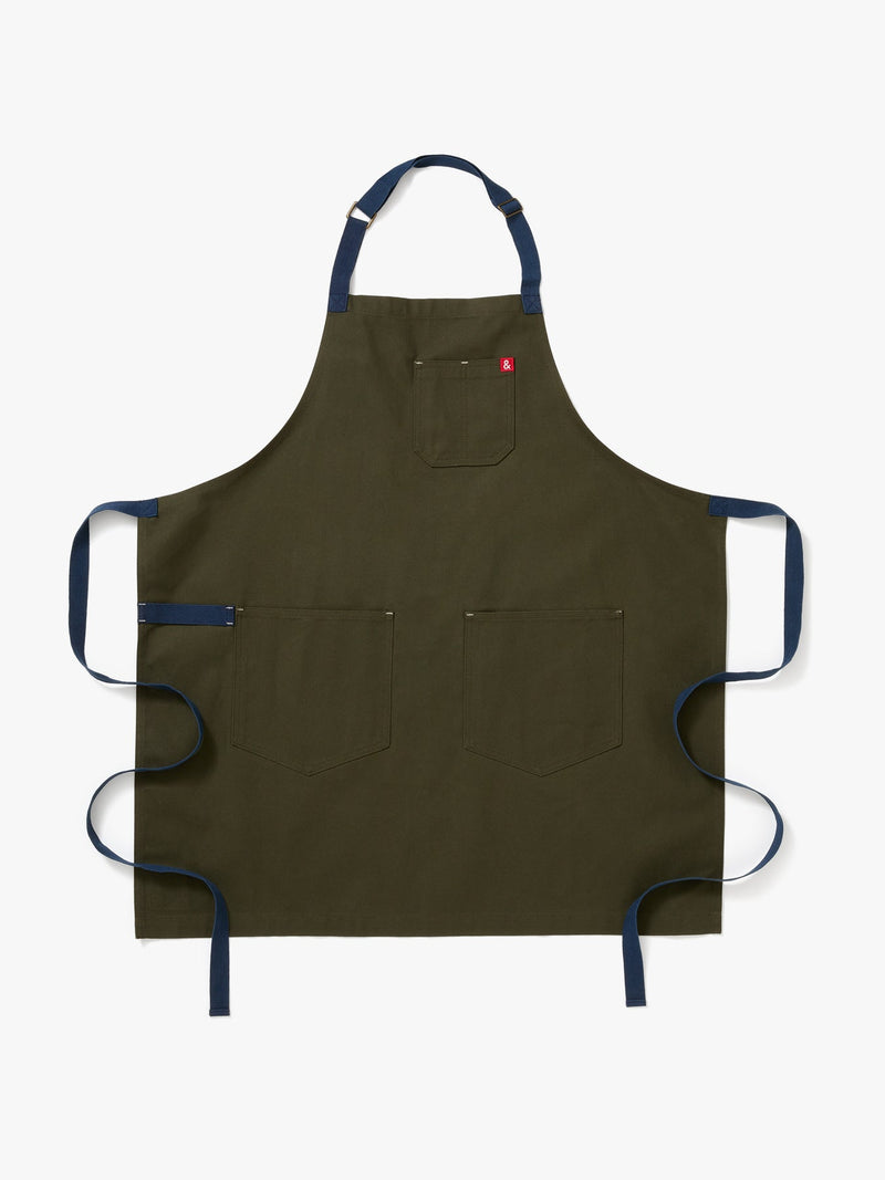 Hedley & Bennett | Essential apron in olive green with navy straps, featuring three patch pockets, laid flat on a white background.