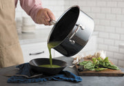 Hestan NanoBond 2qt Saucepan pours vibrant green soup into a black bowl, showcasing its precision pouring and ergonomic design amidst fresh kitchen ingredients.
