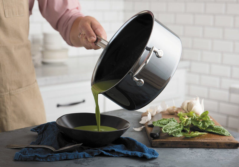 Pouring green soup into a black bowl from a Hestan NanoBond 4qt Saucepan, showcasing its precision pouring spout and ergonomic handle, ideal for culinary perfection.