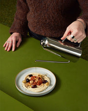 Holcomb Studio Oil Can pouring olive oil onto a plate of food, showcasing its elongated spout and sleek stainless steel design.