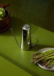 Holcomb Studio Oil Can beside asparagus, showcasing its sleek stainless steel design and elongated spout for precise oil pouring, perfect for kitchen use.