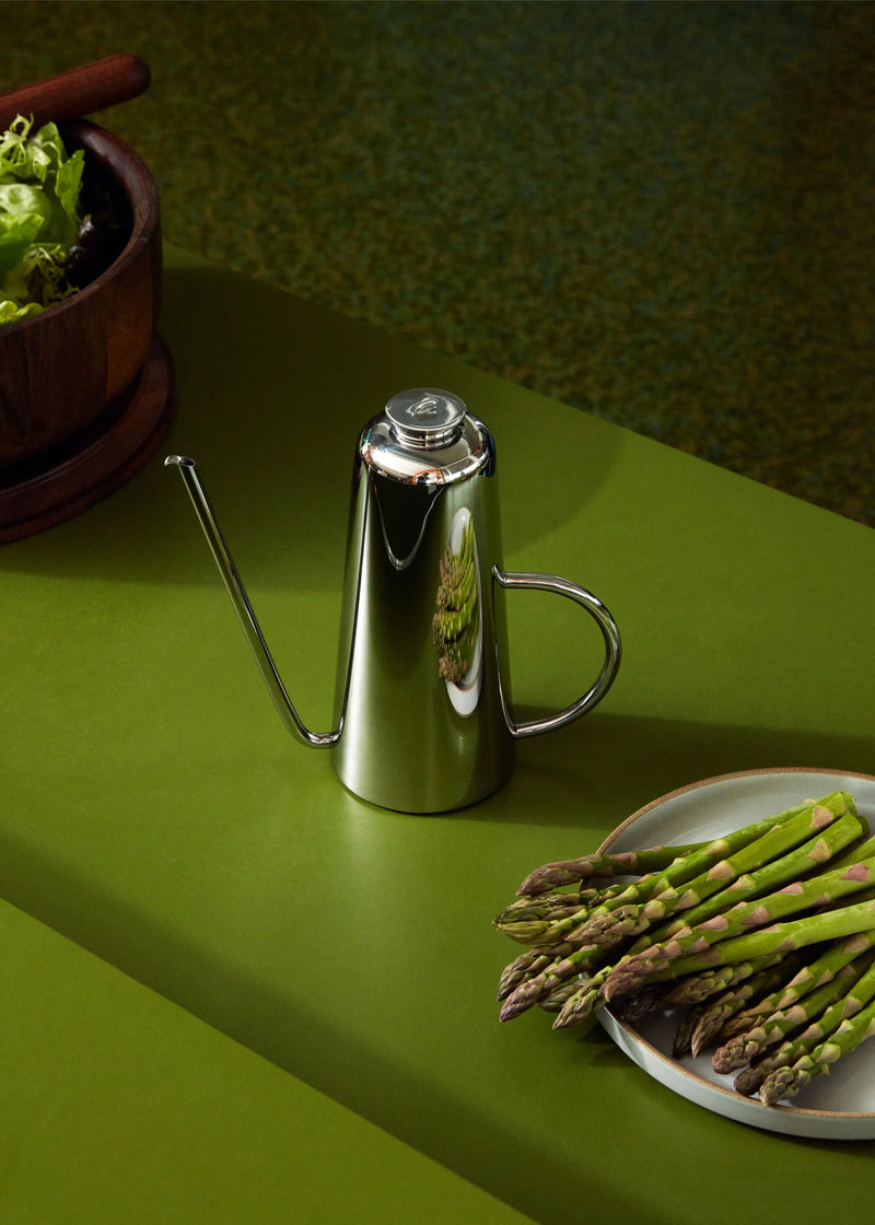 Holcomb Studio Oil Can beside asparagus, showcasing its sleek stainless steel design and elongated spout for precise oil pouring, perfect for kitchen use.