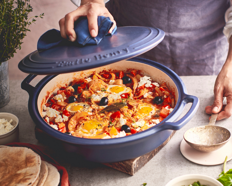 The Emile Henry Modern Classics Loaf Pan, Rouge, 9 x 5, showcased with a shakshuka in a blue casserole, highlights its elegant oven-to-table versatility.