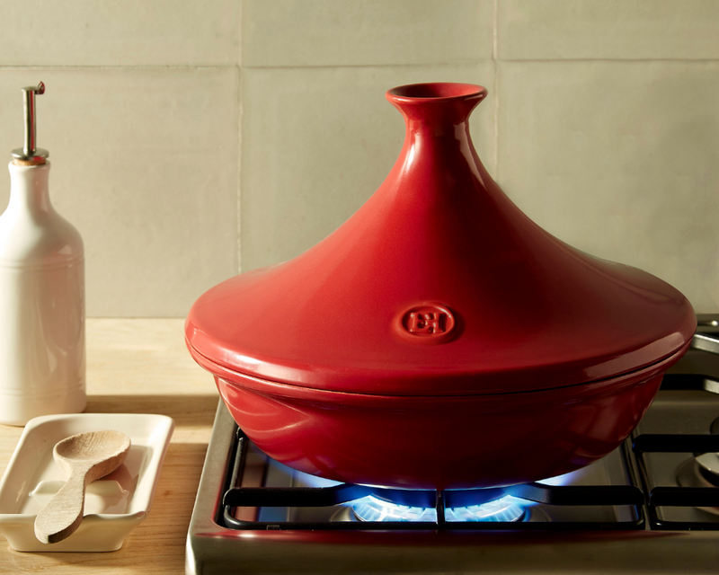 Red conical-lidded tagine on gas stove burner next to oil dispenser and kitchen tools, representing Emile Henry Focaccia + Detroit Pizza Pan, 16 x 12.5, Burgundy.