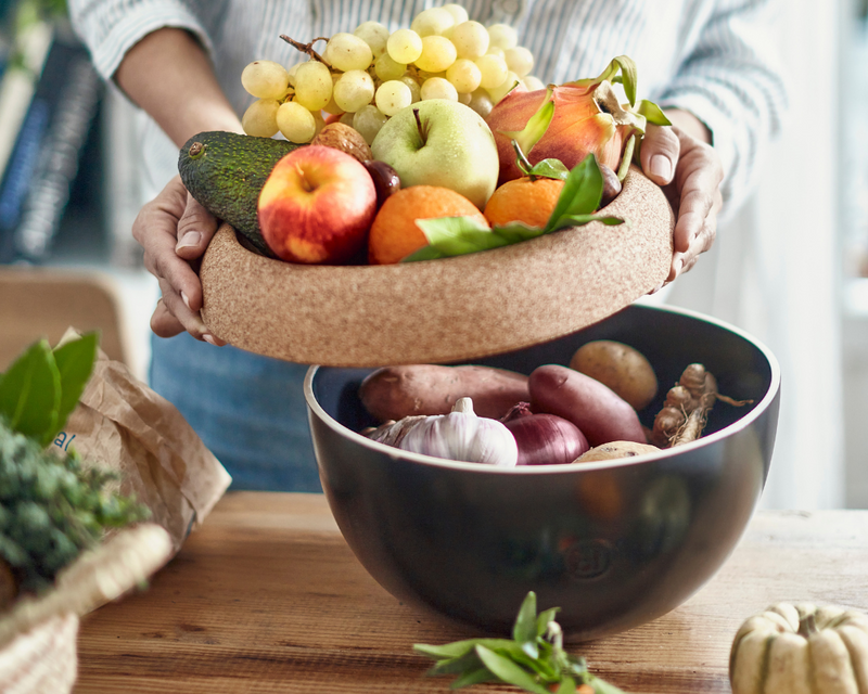 Two-tier produce keeper on countertop with fruits and root vegetables, highlighting a person lifting the cork tray lid; related to Emile Henry Modern Classics Loaf Pan, Rouge.