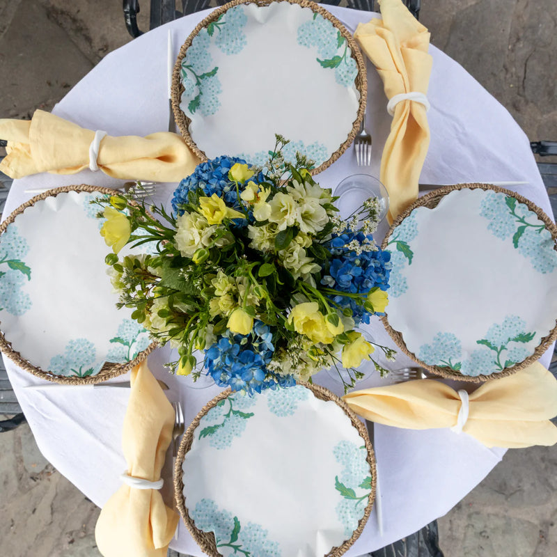 Garden Party Original Flat Plates on a table, adorned with blue hydrangea liners, surrounded by flowers and dishware, perfect for serving summer meals.