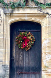 Weston Farms Magnolia Wreath on an old wooden door, featuring lush green and brown leaves with a red bow, enhancing entrance decor.