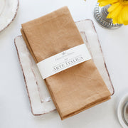Arte Italica & Crown Linen Designs' Harvest Gold linen napkin set, elegantly wrapped, on a ceramic plate with floral accents, enhancing dining aesthetics.