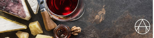 Top-down view of Wine Around the World: France featuring assorted cheeses, red wine, fig jam, walnuts, and a cheese knife on a slate surface.
