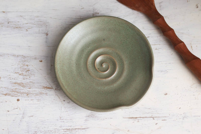 Handmade Gravesco Pottery spoon rest with green spiral pattern on a whitewashed surface, ideal for holding cooking utensils.