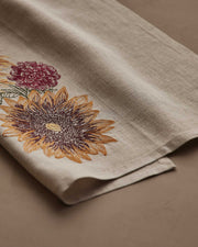 Coral & Tusk - Autumn Sunflower Tea Towel, featuring embroidered sunflower and chrysanthemum, folded on a matching surface, ideal for seasonal kitchen decor.