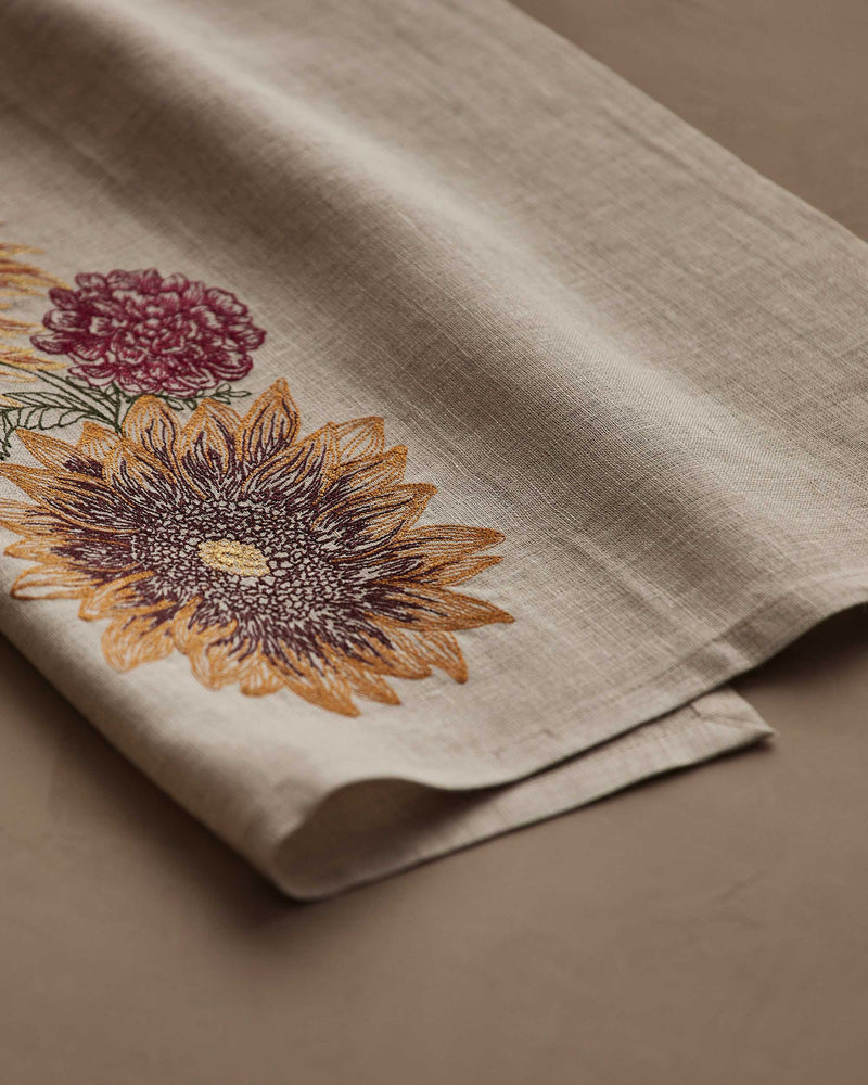 Coral & Tusk - Autumn Sunflower Tea Towel, featuring embroidered sunflower and chrysanthemum, folded on a matching surface, ideal for seasonal kitchen decor.