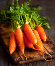 Bentley Seed Co. - Carrot-Nantes 1870: Fresh carrots with leafy tops on a wooden board, ideal for container gardening and cooking enthusiasts.