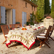Couleur Nature - Gooseberry Red & Green tablecloth on a dining table set with citrus fruits and wine, enhancing a rustic outdoor dining scene.