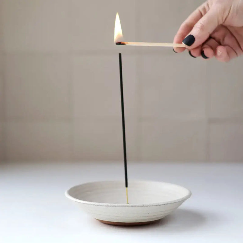 Hand lighting incense on Gravesco Pottery Incense Burner, a ceramic dish designed to catch ash, suitable for standard incense sticks, from Athens Cooks kitchen store.