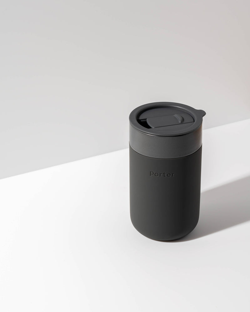 W&P - Ceramic Reusable Coffee Mug 16oz: Charcoal, featuring a silicone sleeve and lid, on a white surface. Ideal for eco-conscious, stylish coffee lovers.