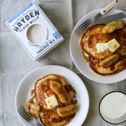 Hayden Flour Mills - White Sonora Pancake Mix with pancakes topped with butter, bananas, and syrup, accompanied by milk. Perfect for delicious, easy breakfast preparation.