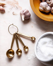 Farmhouse Pottery - Stowe Measuring Spoons: Brushed Gold, arranged on a countertop with garlic and salt, showcasing luxury and precision for kitchen enthusiasts.