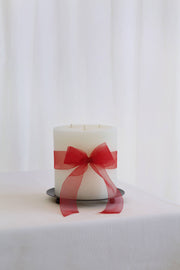 Mo&Co Home - 200h Burn | GRAND Beeswax Pillar Candle | Natural White, featuring three wicks and a red ribbon, on a metal stand.