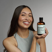 Young woman holding Davids Hydroxi™ oil pulling oral rinse, featuring nano hydroxyapatite, promoting oral health through a natural coconut mint formula.