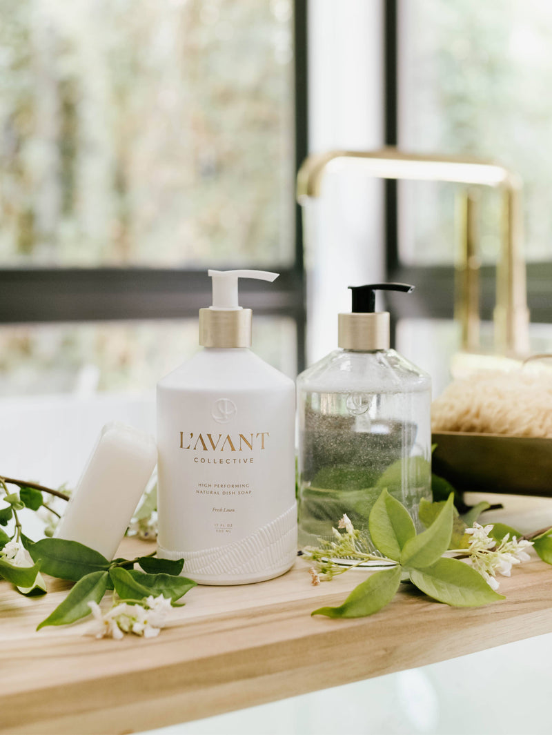 L'AVANT Collective - Fresh Linen High Performing Dish Soap in a stylish matte white glass bottle, showcased on a wooden counter alongside other kitchen essentials.