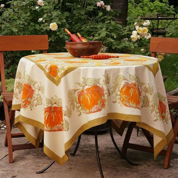 Caravan Home - Pumpkin Orange & Mustard Tablecloth: 71 x 71, handprinted with pumpkins, adorns a garden table, embodying autumnal charm and artisanal craftsmanship.