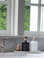 L'AVANT Collective - Fresh Linen Hand Soap in a matte black glass bottle, elegantly displayed on a bathroom counter next to a white bottle.