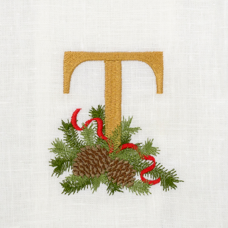 Winter Pine Monogram Towel with gold T, festive evergreen sprigs, and red ribbon embroidery on linen, ideal for gifts or holiday decor.