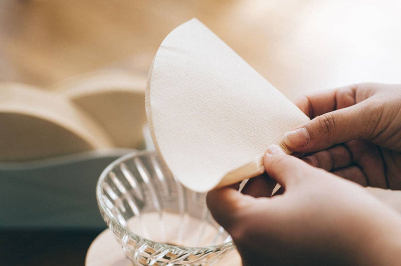 Hands holding HARIO USA - V60 Paper Filters over a glass bowl, showcasing their compatibility with V60 drippers for optimal coffee brewing.