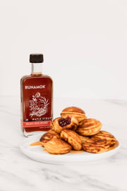 Runamok Holiday Spice Infused Maple Syrup 250ml bottle beside mini pancake puffs on a white plate, with syrup pooled underneath. Perfect for festive gifting at Athens Cooks.