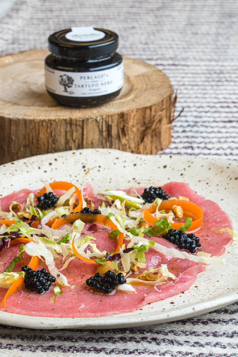 TartufLanghe - Truffle Perlage Caviar-Style Pearls elegantly adorns beef carpaccio with truffle pearls, carrots, greens, nuts, enhancing this gourmet dish's sophistication and flavor.