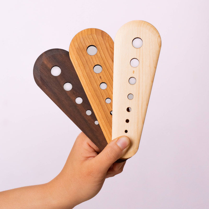 Hand holding three maple wood Collin Garrity herb stripper swatches, showcasing circular cut-outs for stripping herbs and scraping seeds, limited-release by Athens Cooks.