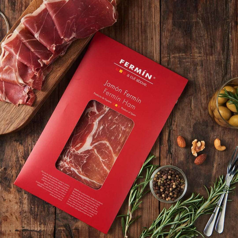 Casacella Foods - Fermin Serrano Ham Cured 18 Months 2 oz, elegantly displayed with sliced ham, nuts, olives, and rosemary, ideal for a charcuterie-style snack.
