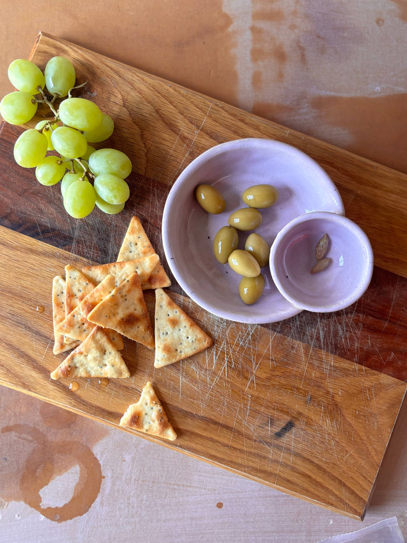 Handmade ROB Ceramics Olive Serving Bowl with attached pit dish, holding green olives, surrounded by grapes and crackers on a wooden board. Ideal for entertaining.