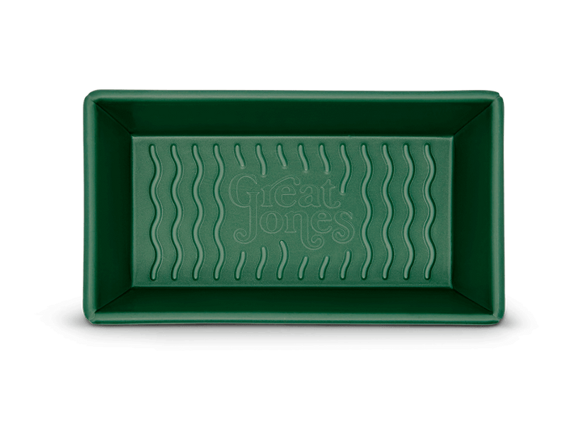 Great Jones | Breadwinner - Raspberry, a green rectangular loaf pan with a wavy, corrugated bottom, designed for nonstick, scratch-resistant baking.