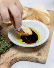 Zia Pia - Foglie Extra Virgin Olive Oil by Galantino with bread, balsamic swirl, rosemary, and cheese on a cutting board.