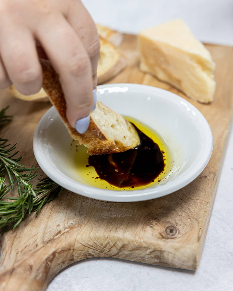 Zia Pia - Foglie Extra Virgin Olive Oil by Galantino with bread, balsamic swirl, rosemary, and cheese on a cutting board.